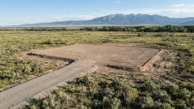 Finished rural house pad connected to a graded driveway on undeveloped Costilla County property