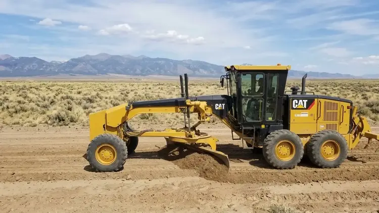 Rural gravel access road being shaped by a yellow tracked excavator across open undeveloped land in Costilla County, Colorado