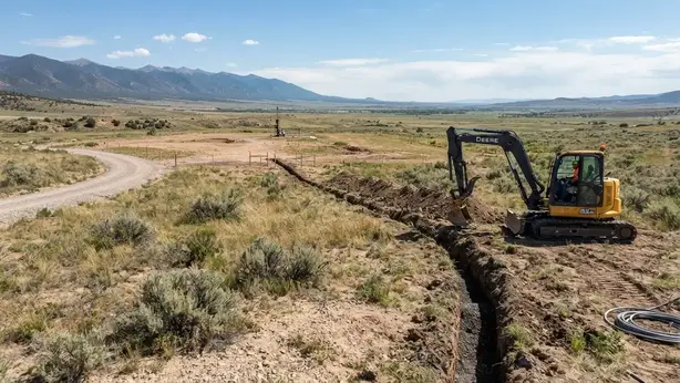 Rural utility trench serving a developing homesite with coordinated well, septic, driveway, and underground infrastructure